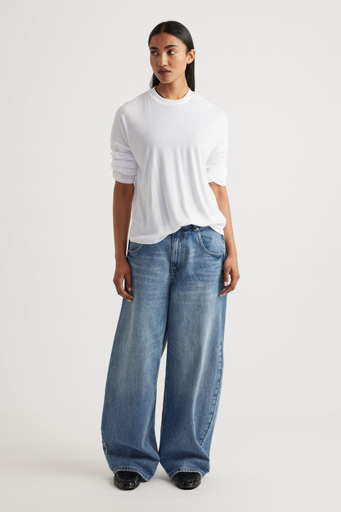 Woman wearing a relaxed white long sleeve rib top paired with loose fit wide-leg blue denim jeans and black shoes