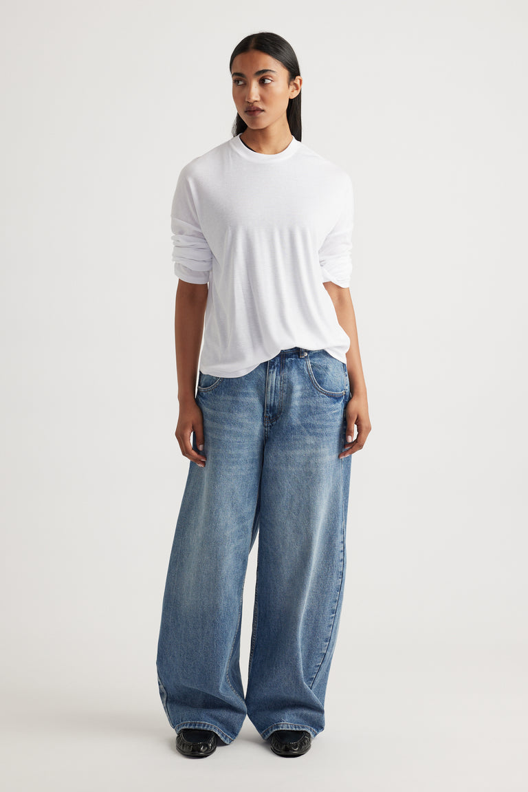 Woman wearing a relaxed white long sleeve rib top paired with loose fit wide-leg blue denim jeans and black shoes