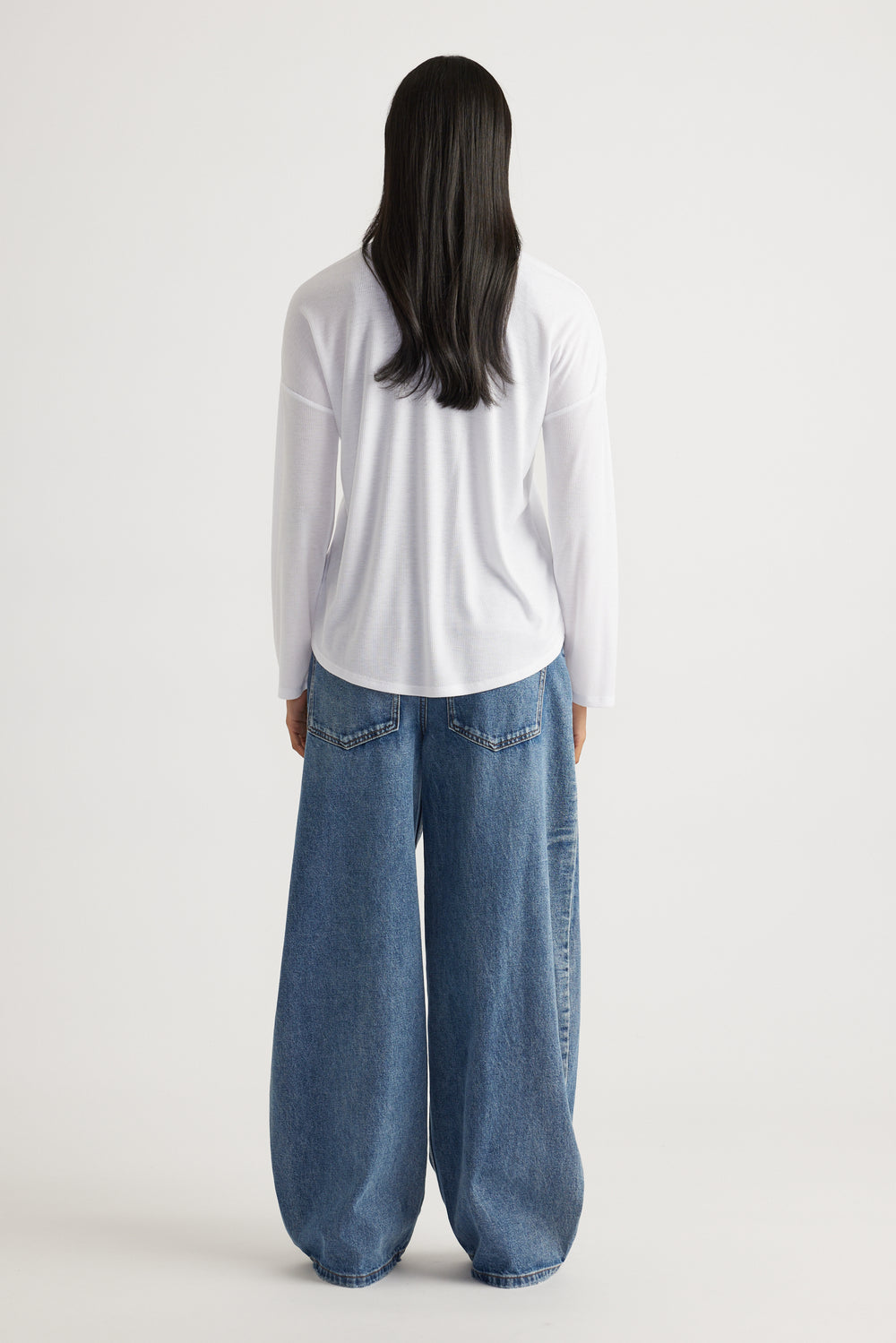 Woman shown from behind wearing a relaxed white ribbed long sleeve top paired with wide-leg blue denim jeans