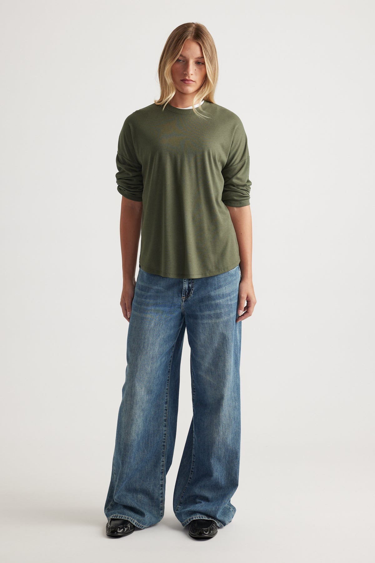 Woman wearing a relaxed forest green ribbed long sleeve top paired with wide-leg blue denim jeans and black shoes