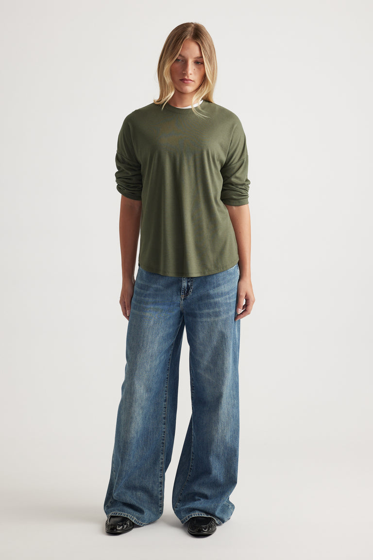 Woman wearing a relaxed forest green ribbed long sleeve top paired with wide-leg blue denim jeans and black shoes