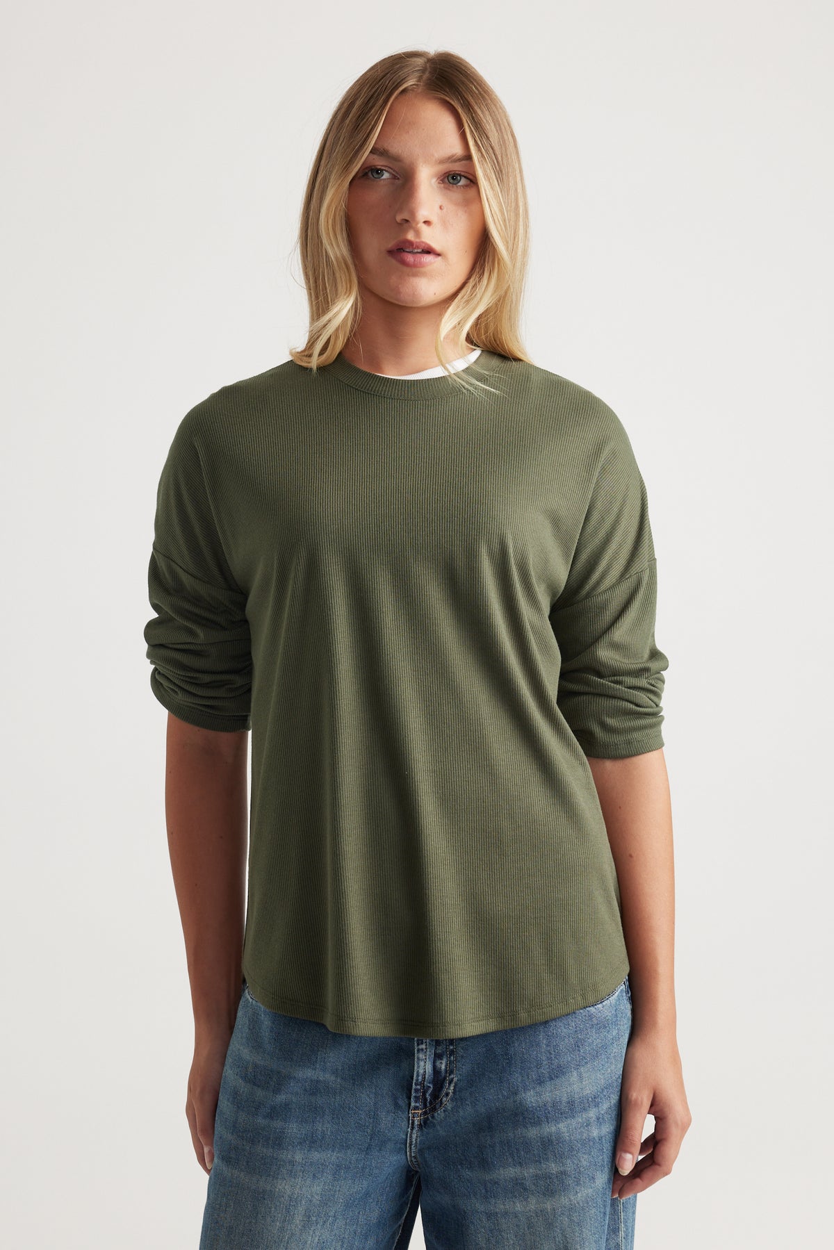 Woman wearing a soft olive green ribbed long sleeve top with a relaxed fit, paired with casual mid-blue jeans