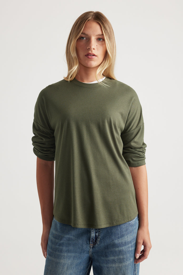 Woman wearing a soft olive green ribbed long sleeve top with a relaxed fit, paired with casual mid-blue jeans