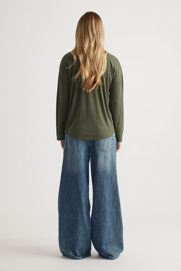 Woman wearing a relaxed fit long sleeve rib top in olive green paired with wide-leg blue denim jeans viewed from behind
