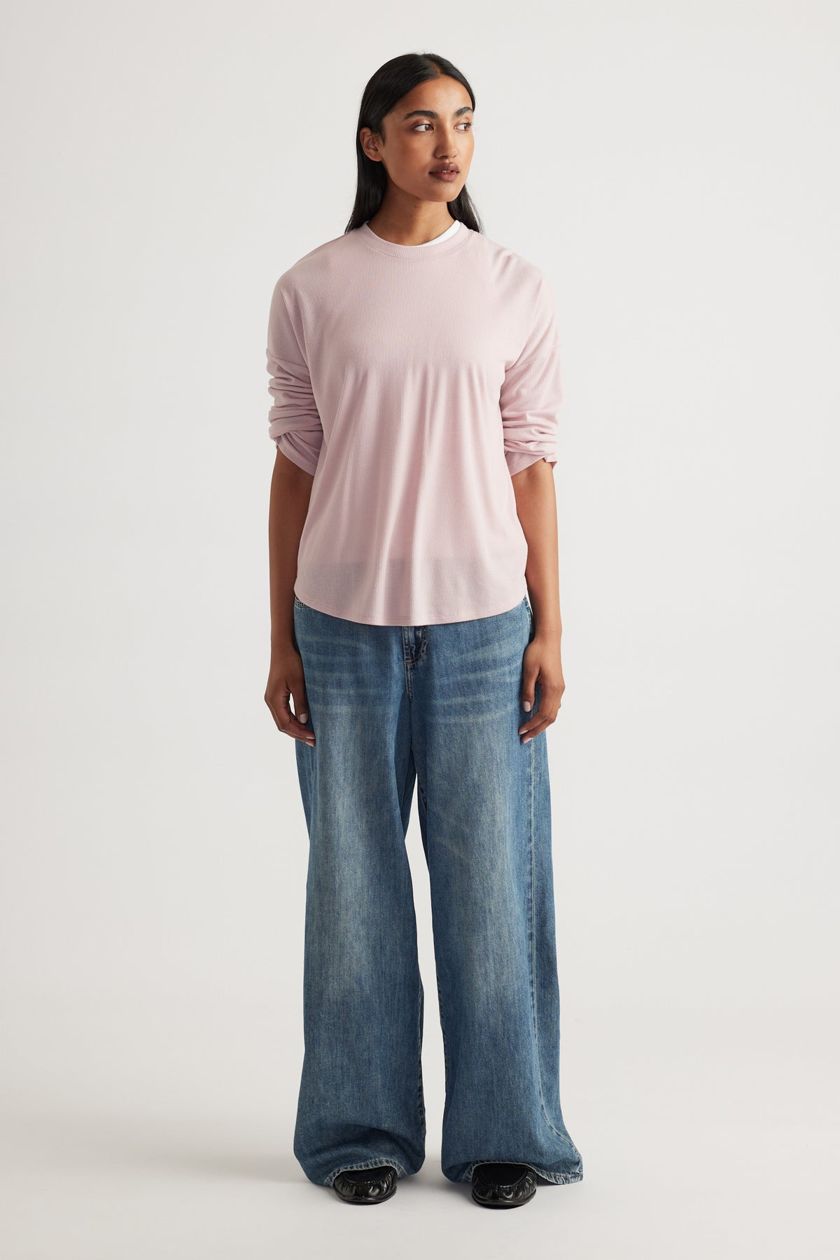 Woman wearing a soft pink long sleeve rib top paired with relaxed wide-leg mid-blue denim jeans and black shoes