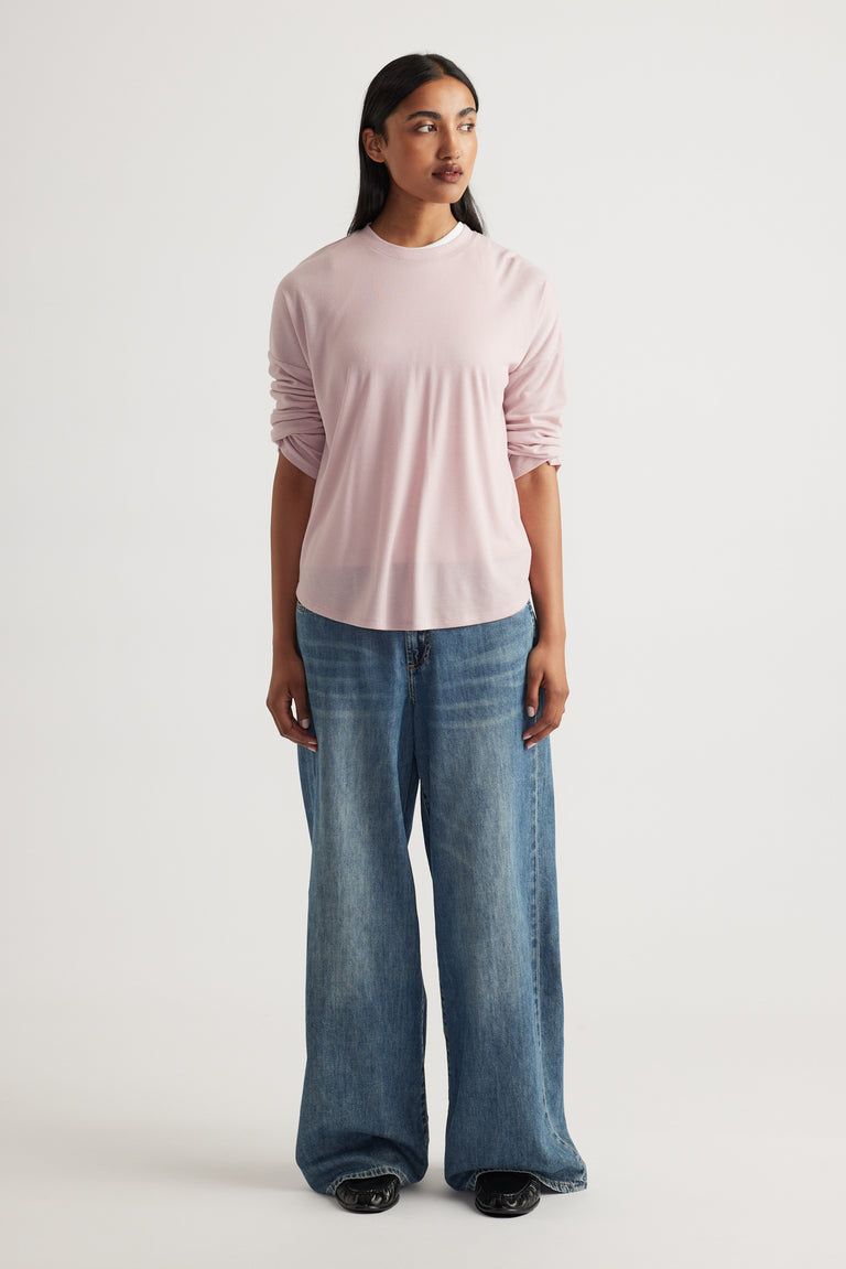 Woman wearing a soft pink long sleeve rib top paired with relaxed wide-leg mid-blue denim jeans and black shoes