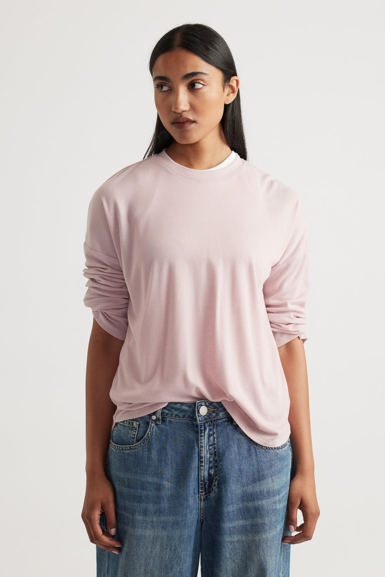 Woman wearing a soft pink long sleeve top with subtle ribbed texture paired with relaxed mid-blue denim jeans
