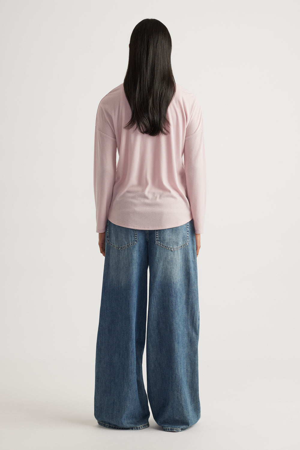 Woman seen from behind wearing a soft pink long sleeve rib top paired with wide-leg blue denim jeans for a relaxed fit