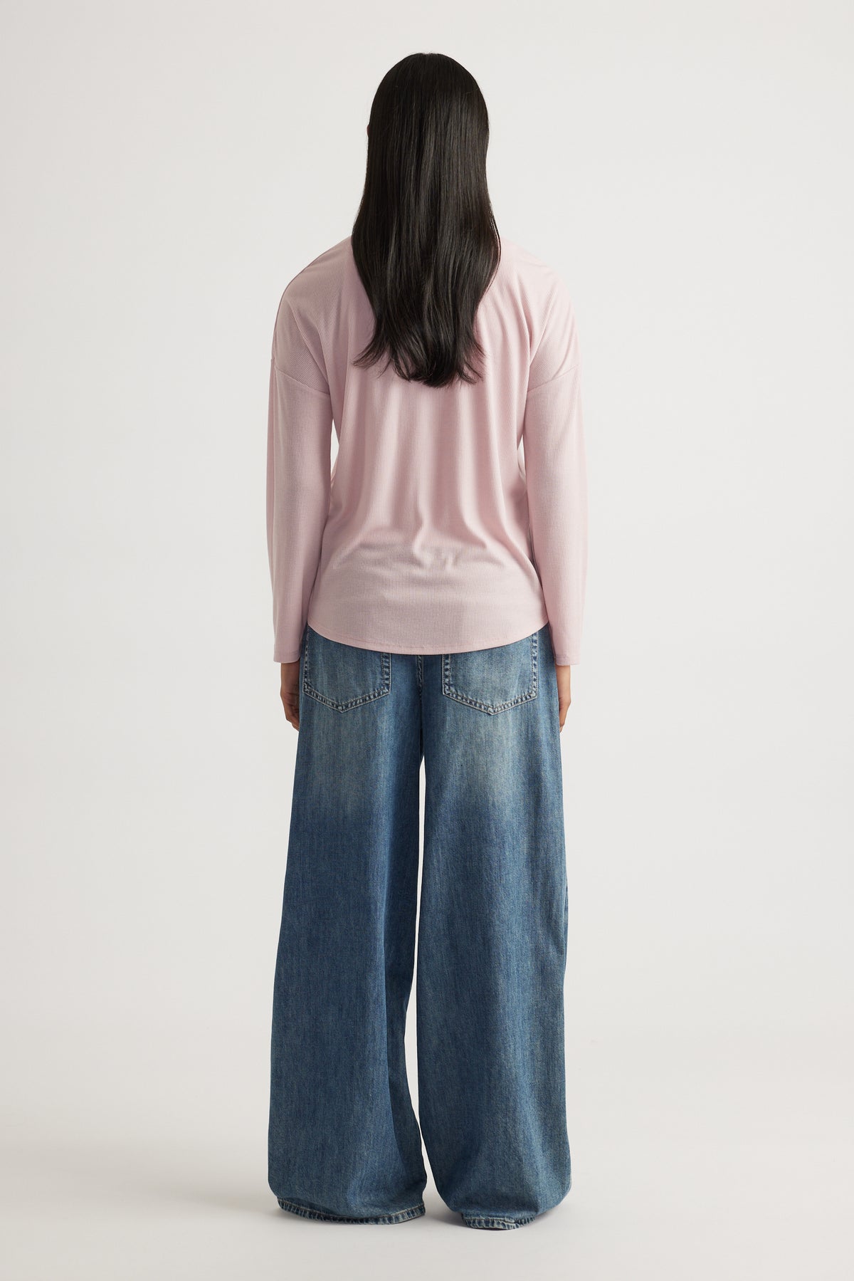 Woman seen from behind wearing a soft pink long sleeve rib top paired with wide-leg blue denim jeans for a relaxed fit