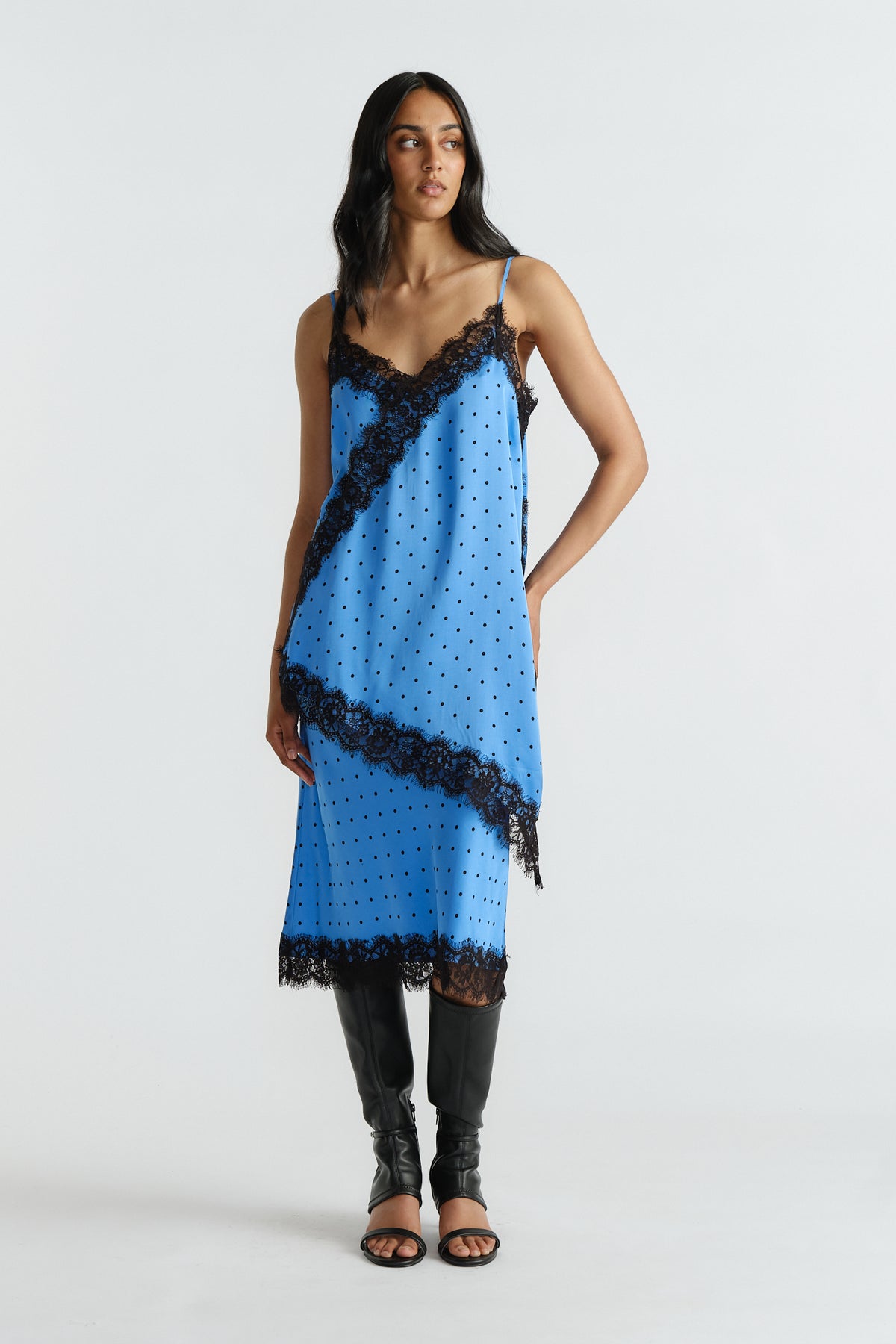 Woman wearing a blue slip tunic with black lace trim and polka dots paired with matching skirt and black knee-high boots.