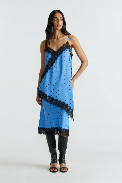 Woman wearing a blue slip tunic with black lace trim and polka dots paired with matching skirt and black knee-high boots.