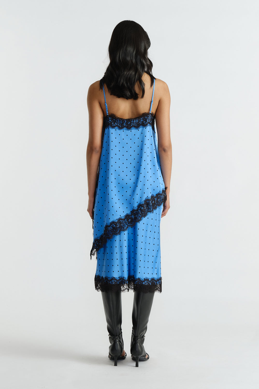 Woman wearing a blue slip dress with black lace trim and polka dots, styled with black knee-high boots, back view.