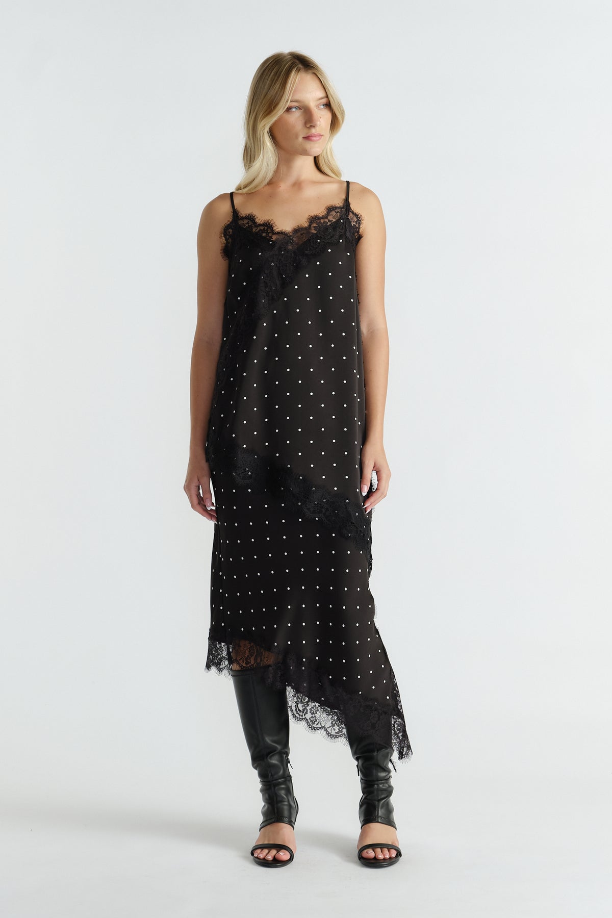 Woman wearing a black lace-trimmed tunic with thin straps and polka dot print paired with knee-high black boots