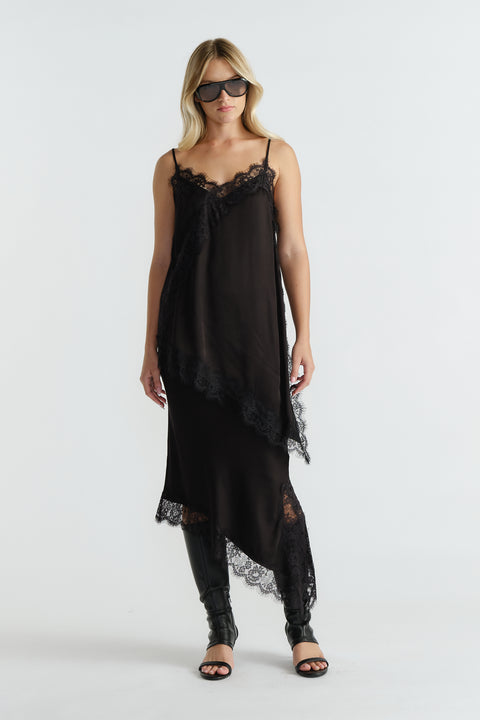 Woman wearing a black lace-trimmed slip dress with asymmetrical hem paired with knee-high boots and sunglasses