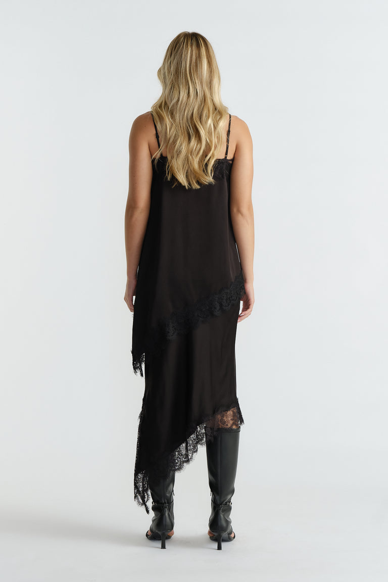 Back view of a woman wearing a black lace-trimmed tunic dress with an asymmetric hem and knee-high boots.