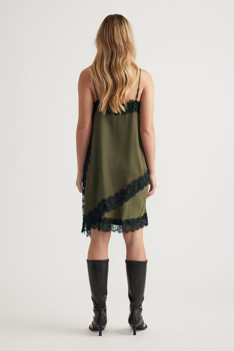 Woman wearing an olive lace-trimmed slip dress with thin straps paired with mid-calf black boots, viewed from behind