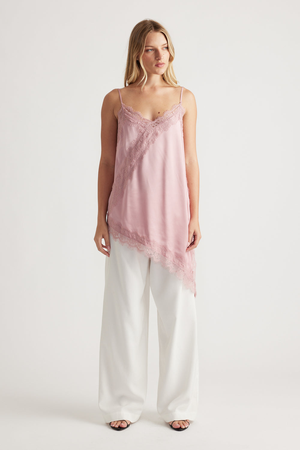 Woman wearing a soft pink lace-trimmed tunic with an asymmetric hem paired with wide-leg white pants for a chic look