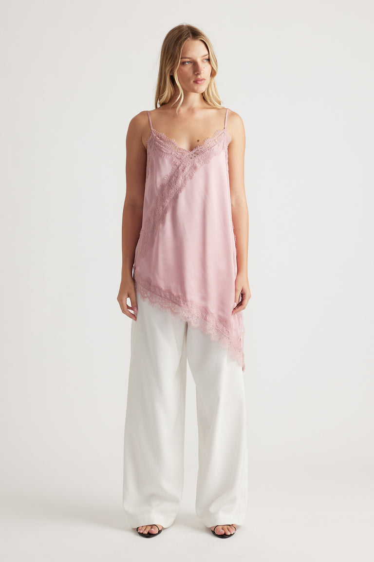 Woman wearing a soft pink lace-trimmed tunic with an asymmetric hem paired with wide-leg white pants for a chic look