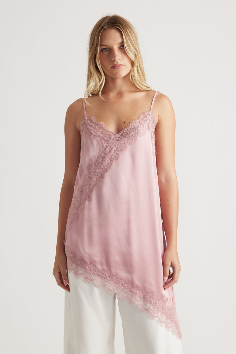 Woman wearing a soft pink lace-trimmed tunic with an asymmetrical hem paired with white wide-leg pants