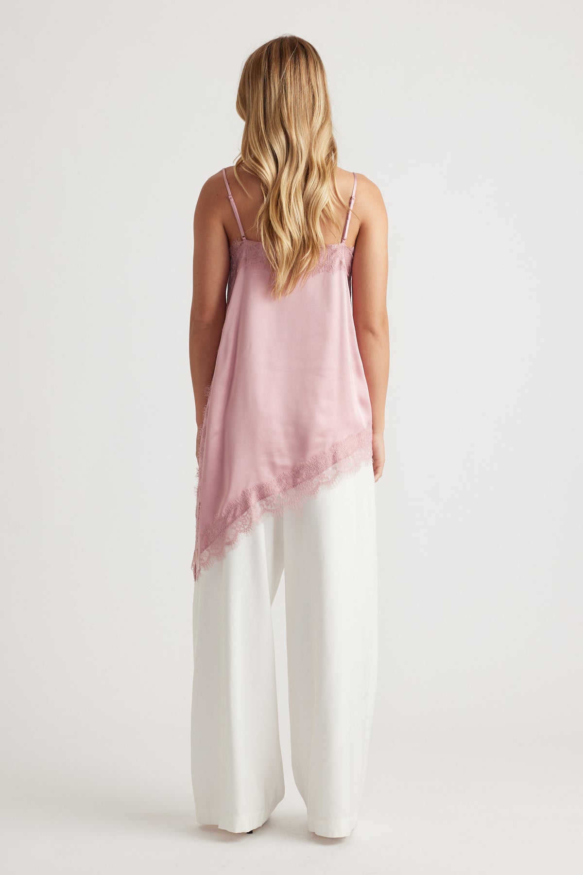 Woman wearing a soft peony pink lace-trimmed tunic with thin straps paired with flowing white wide-leg pants