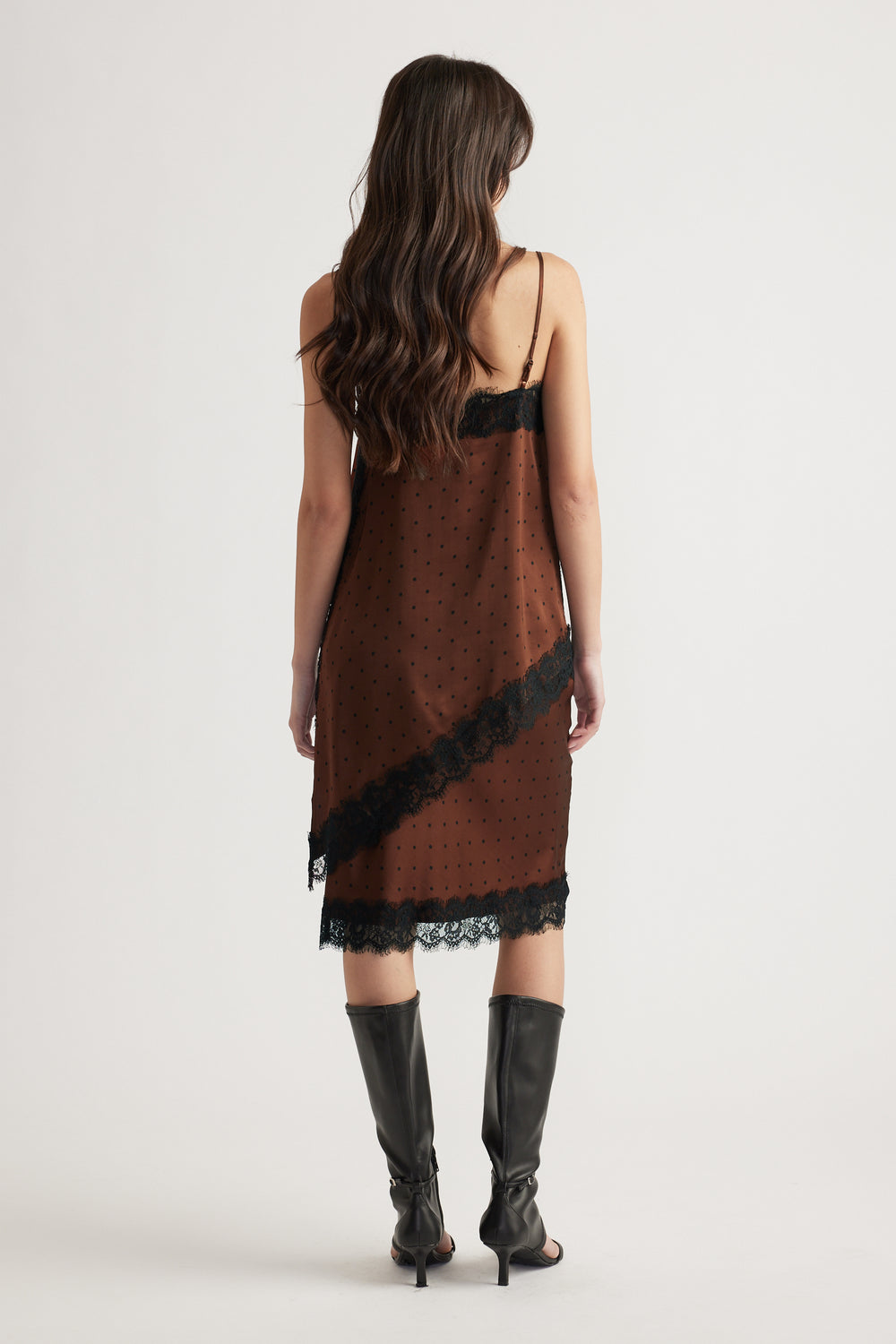 Woman wearing a brown slip dress with black lace trim, thin straps, and knee-high black heeled boots viewed from behind