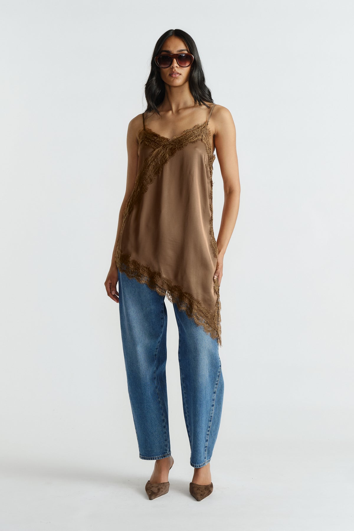 Woman wearing brown lace-trimmed tunic with adjustable straps paired with loose mid-blue denim jeans and pointed flats