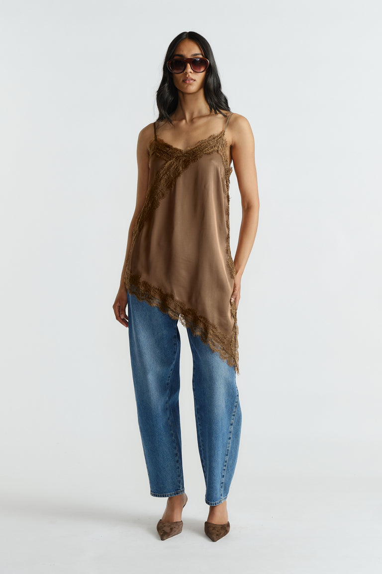 Woman wearing brown lace-trimmed tunic with adjustable straps paired with loose mid-blue denim jeans and pointed flats