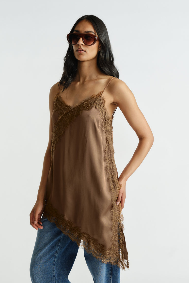 Woman wearing a brown lace-trimmed tunic with thin straps and asymmetric hem paired with blue denim jeans and sunglasses