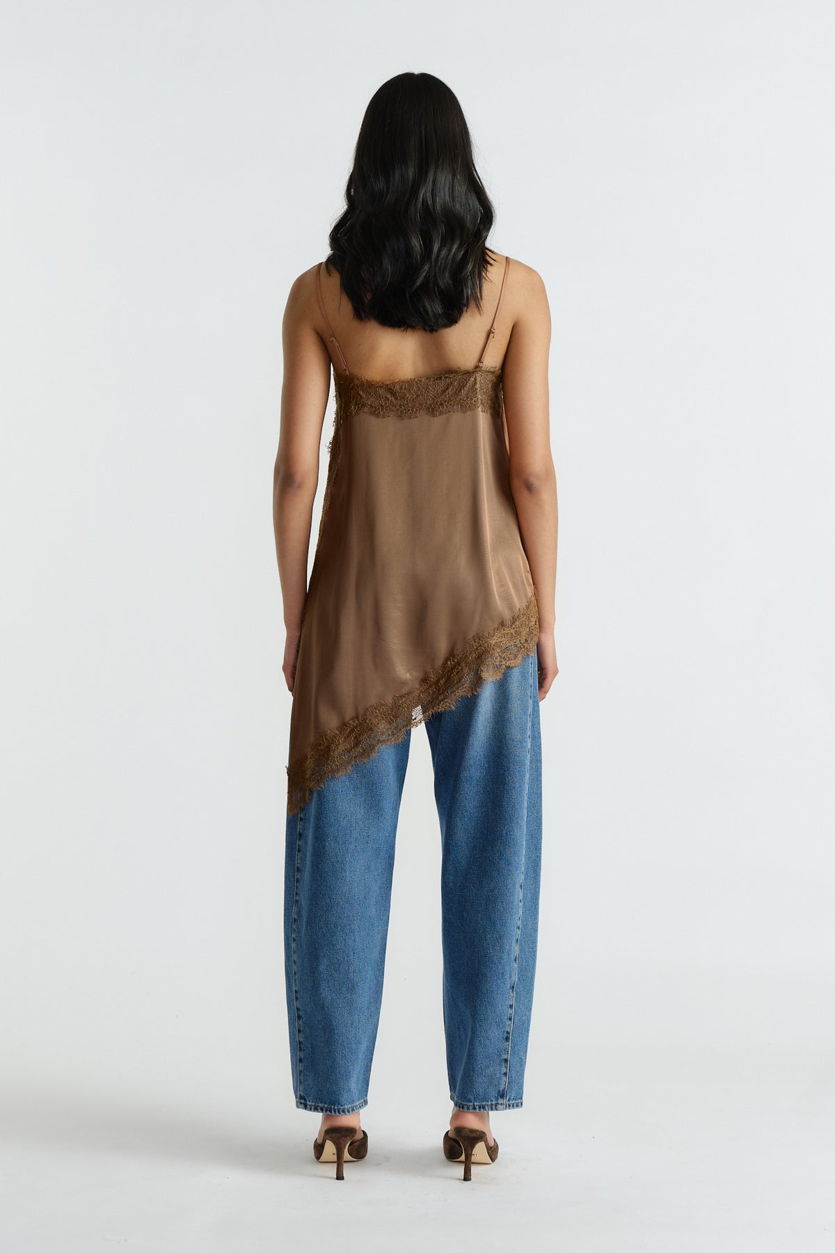 Woman wearing a brown lace trim tunic with adjustable straps paired with loose blue denim jeans and heels viewed from behind