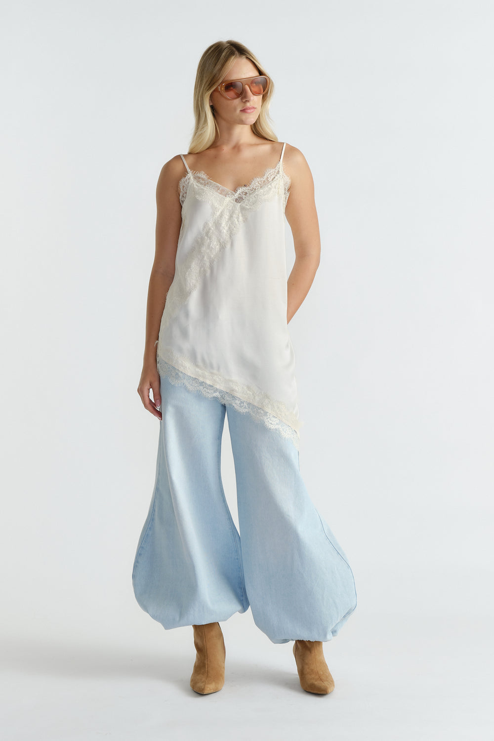 Woman wearing an ivory lace-trimmed tunic paired with wide-leg light denim pants and tan suede ankle boots.