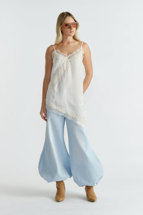Woman wearing an ivory lace-trimmed tunic paired with wide-leg light denim pants and tan suede ankle boots.