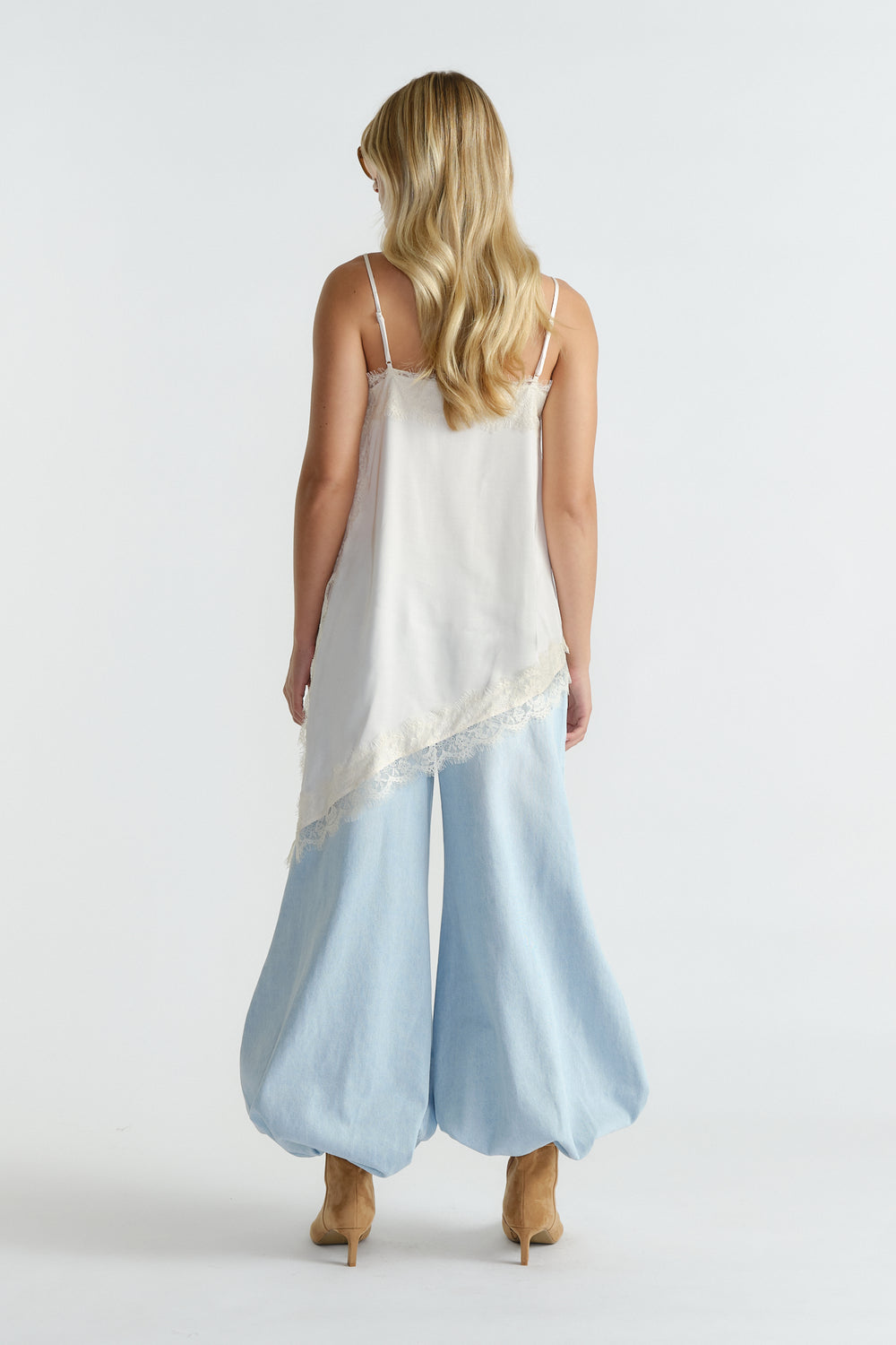 Back view of woman with long blonde hair wearing a white lace-trimmed tunic and wide-leg light blue denim pants