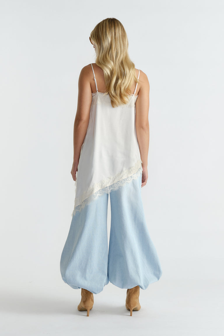 Back view of woman with long blonde hair wearing a white lace-trimmed tunic and wide-leg light blue denim pants