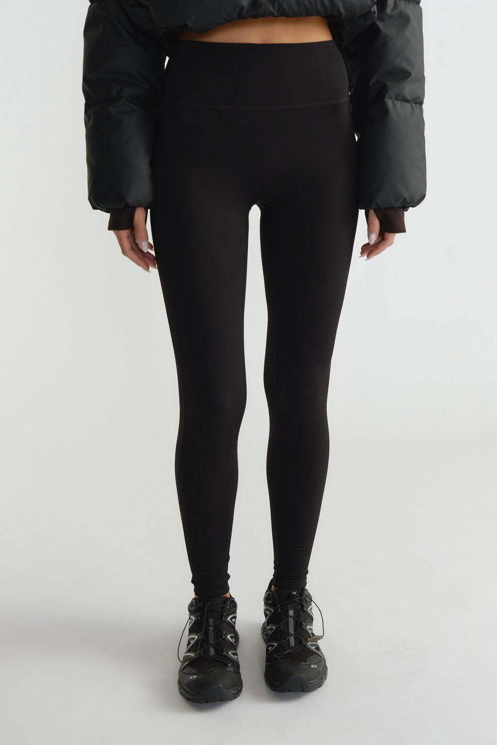 High-waisted black leggings with a smooth matte finish paired with sporty black sneakers and a cropped puffer jacket.