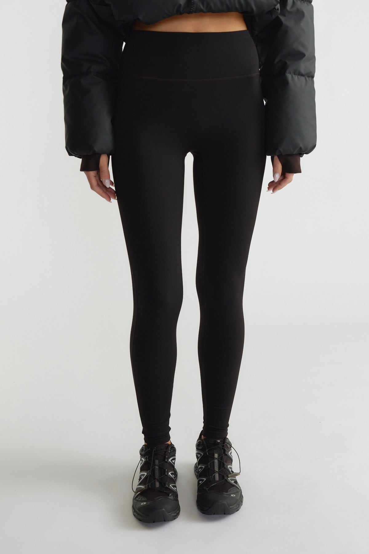 High-waisted black leggings with a smooth matte finish paired with sporty black sneakers and a cropped puffer jacket.