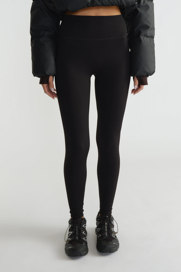High-waisted black leggings with a smooth matte finish paired with sporty black sneakers and a cropped puffer jacket.