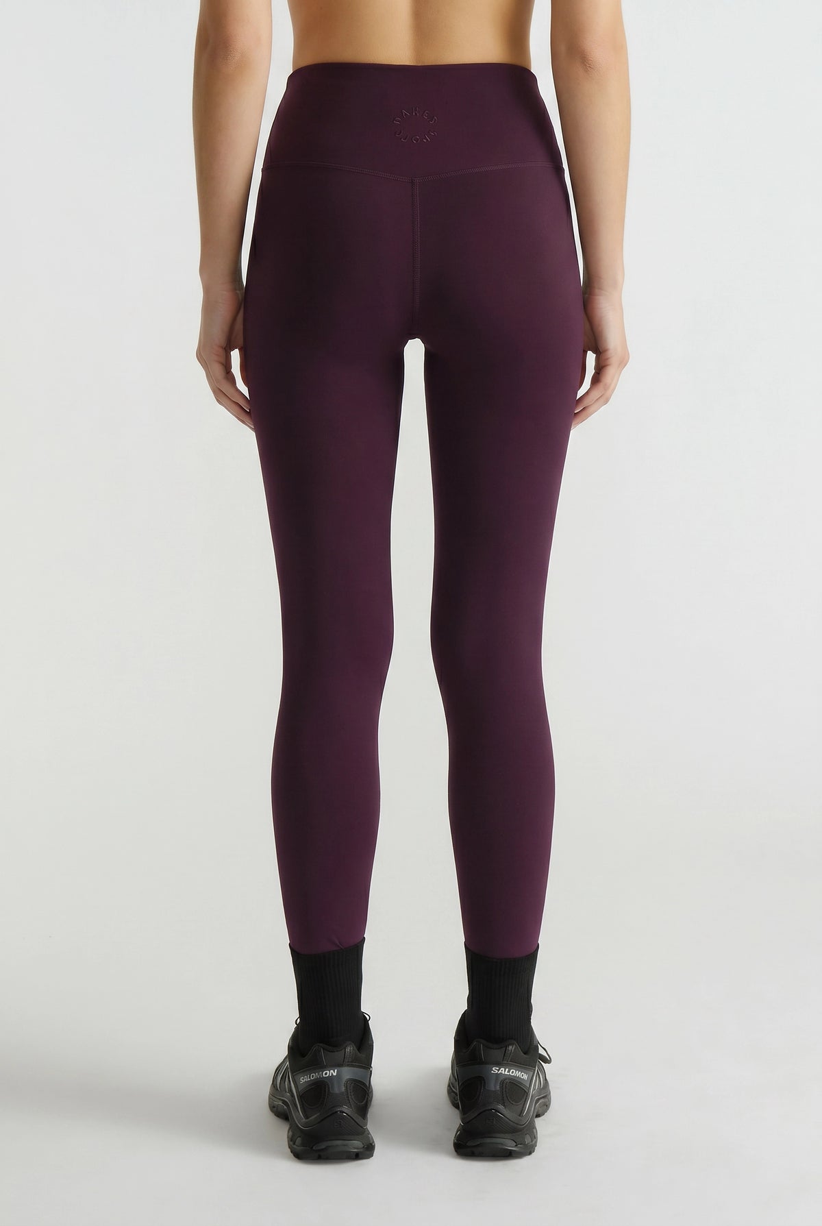 Back view of woman wearing plum-colored high-waisted leggings paired with black sneakers and ankle socks
