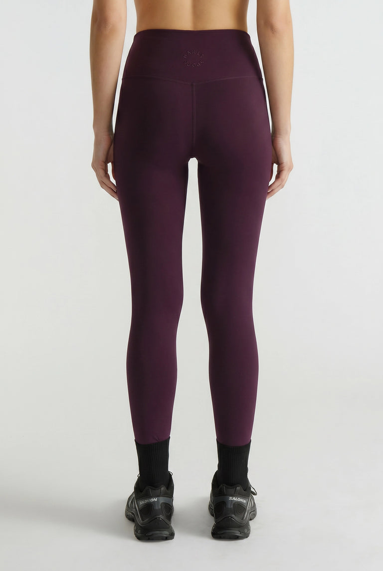 Back view of woman wearing plum-colored high-waisted leggings paired with black sneakers and ankle socks