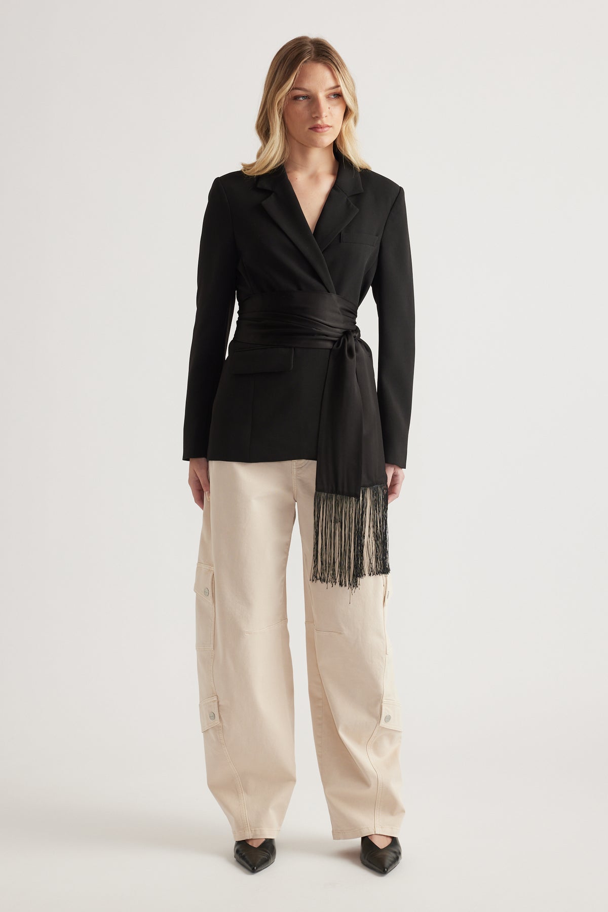 Woman wearing cream barrel leg cargo pants with a black wrap blazer and pointed heels
