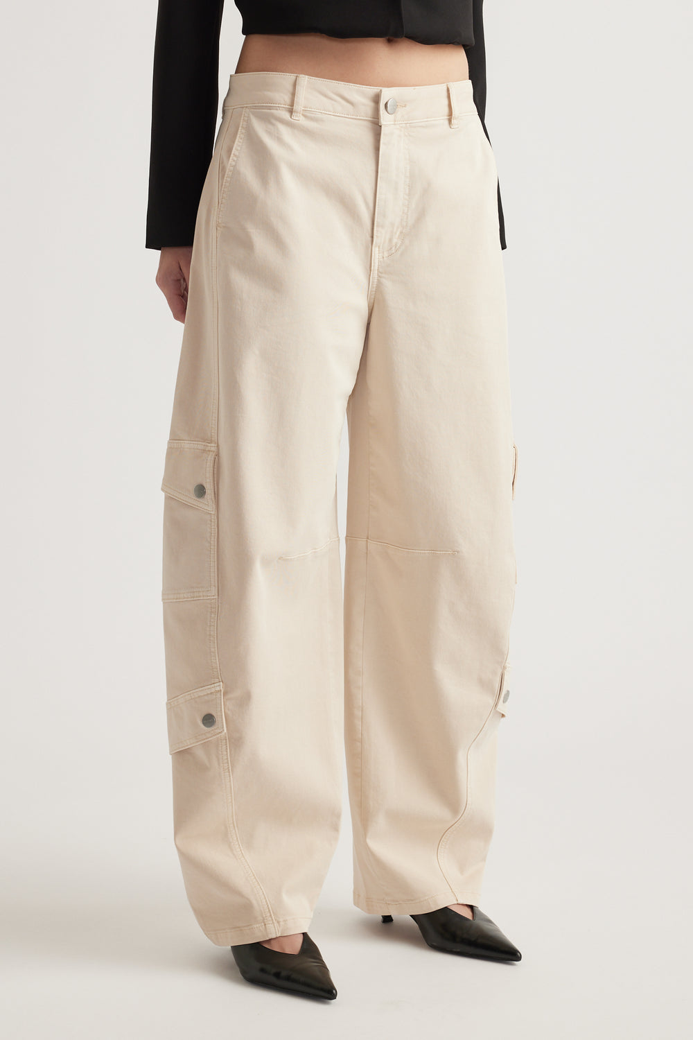 Woman wearing cream barrel-leg cargo pants with utility pockets, a cropped black top and pointed flats