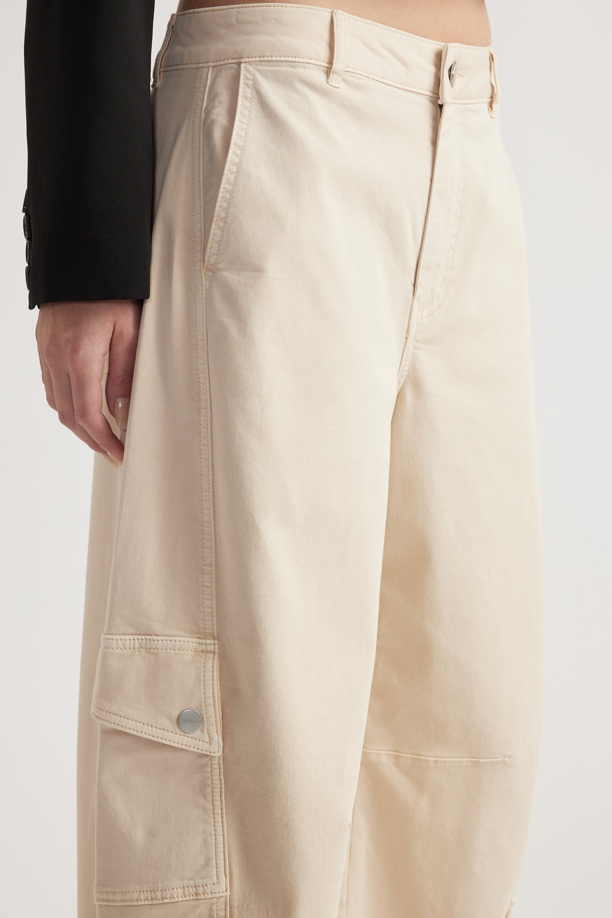 Woman wearing cream barrel leg cargo pants with flap cargo pockets and a black blazer