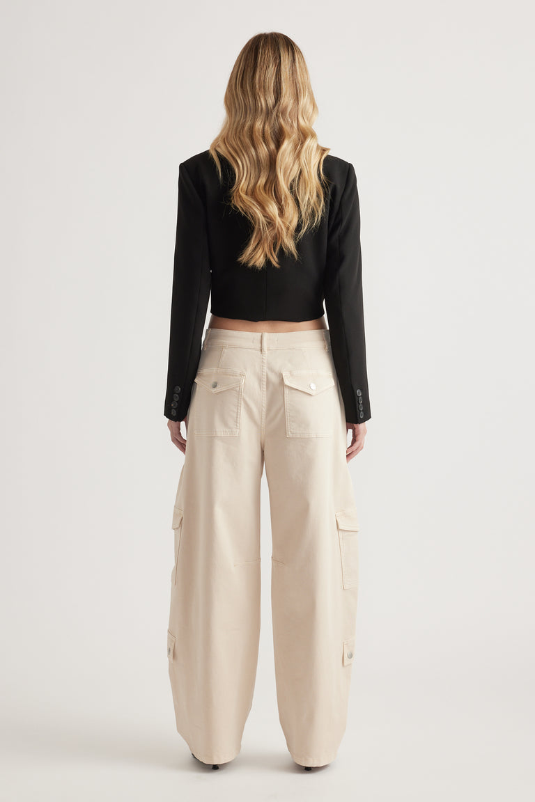 Back view of woman wearing cream barrel leg cargo pants with cargo pockets and a cropped black blazer