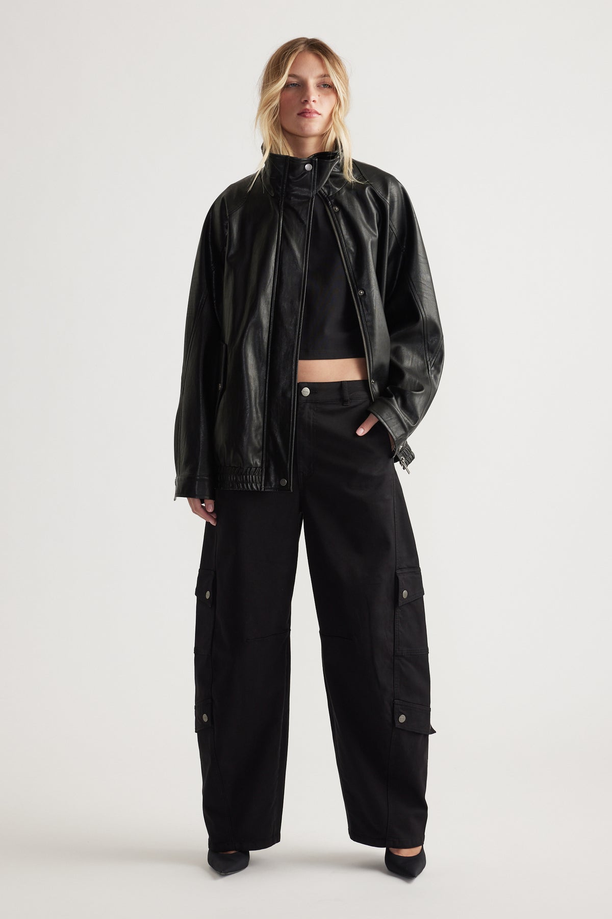 Woman wearing black cargo pants with flap pockets paired with a cropped top and relaxed leather jacket for a bold look