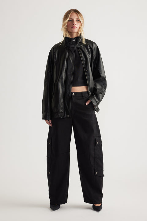 Woman wearing black cargo pants with flap pockets paired with a cropped top and relaxed leather jacket for a bold look