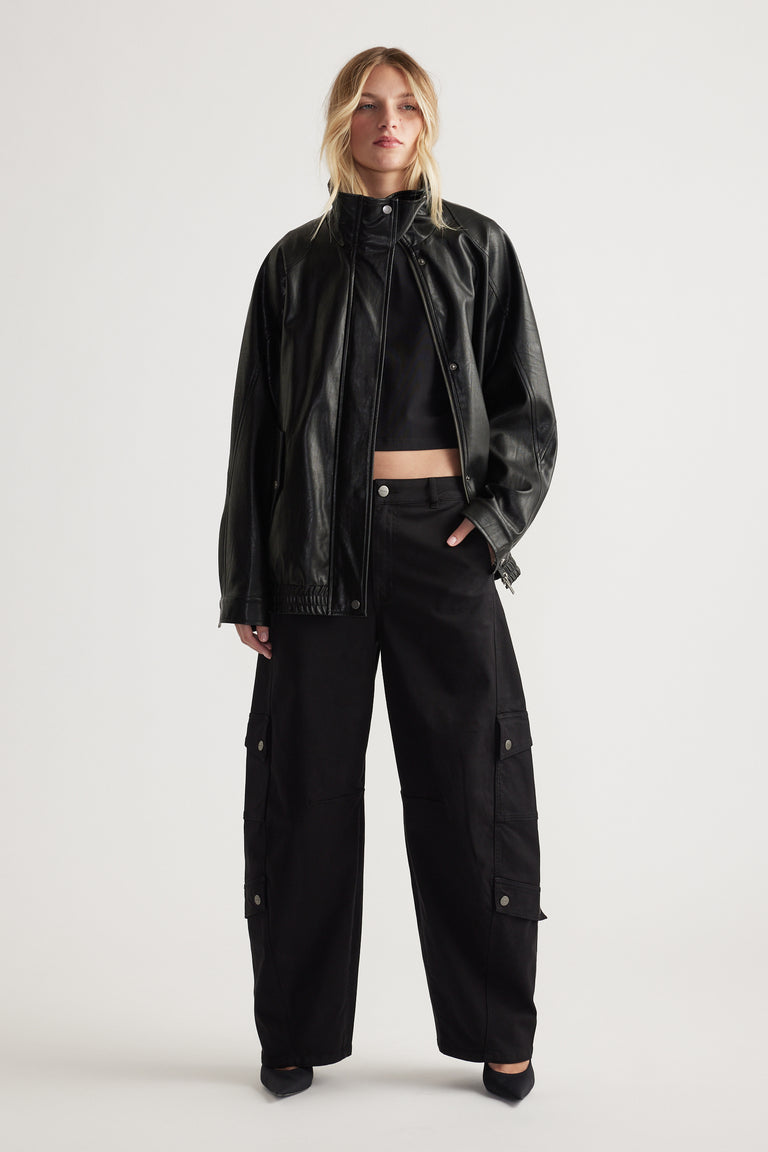 Woman wearing black cargo pants with flap pockets paired with a cropped top and relaxed leather jacket for a bold look