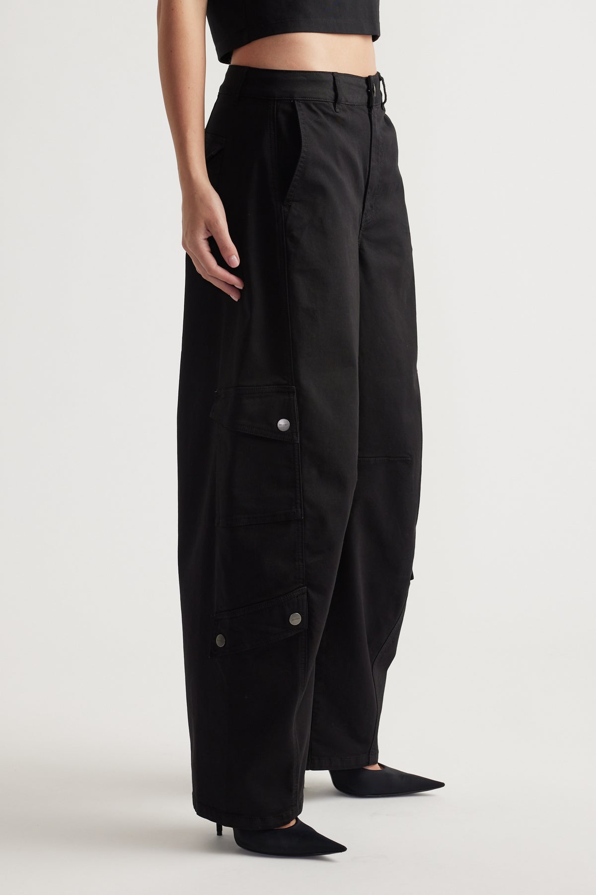 Woman wearing relaxed black wide-leg cargo pants with flap pockets and subtle metal snap details