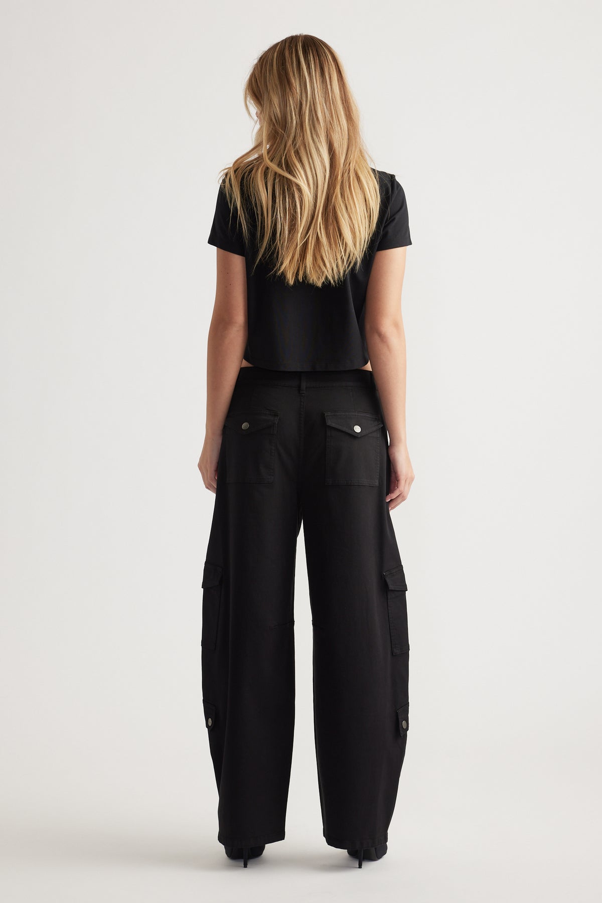 Woman wearing black cargo pants with buttoned back and side pockets paired with a fitted black cropped tee