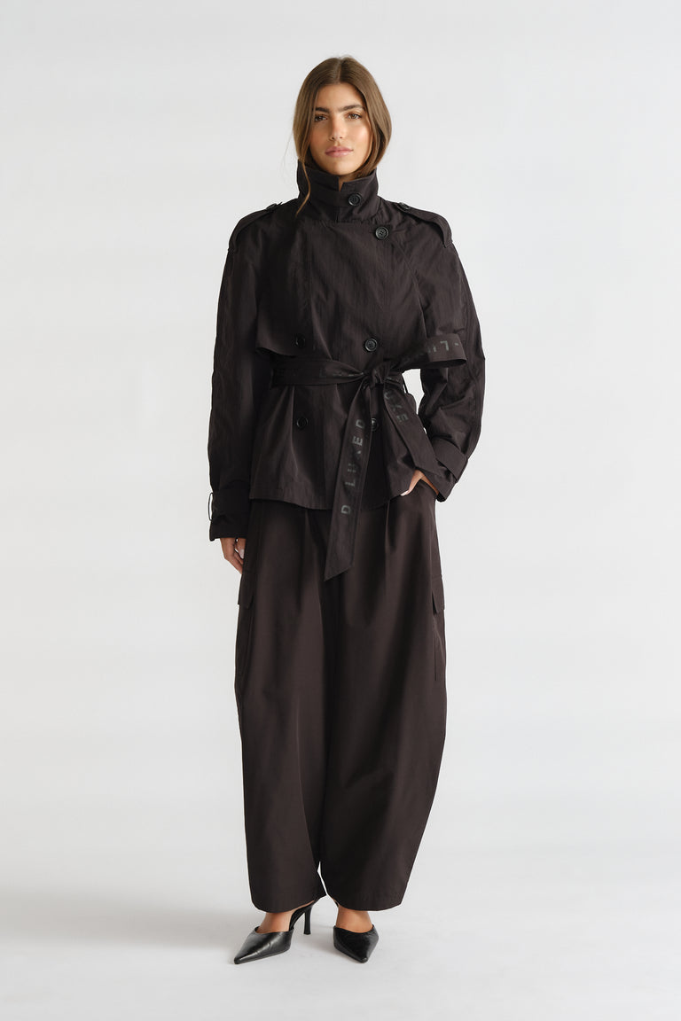 Woman wearing a black cropped trench with a waist tie, paired with wide-leg trousers and pointed black heels.