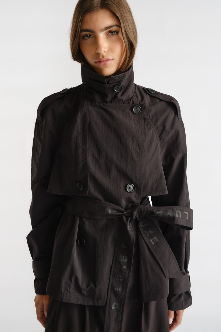Woman wearing a sleek black cropped trench with button details and a tied waist belt for a modern, polished look