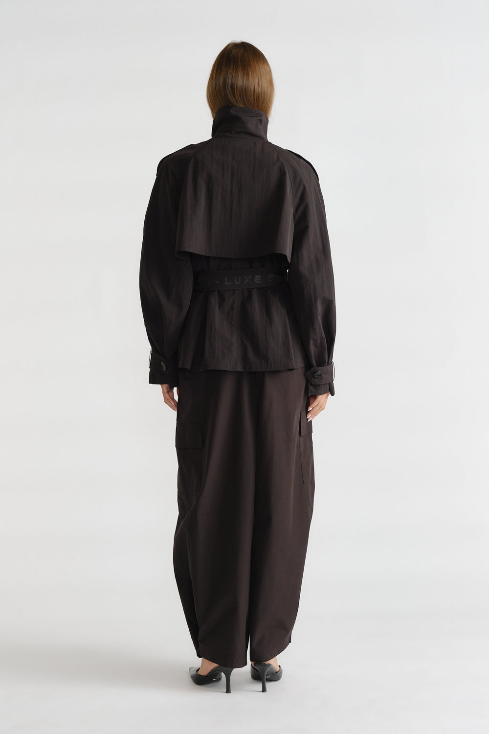Back view of woman wearing a cropped black nylon trench jacket with a belted waist and wide-legged pants